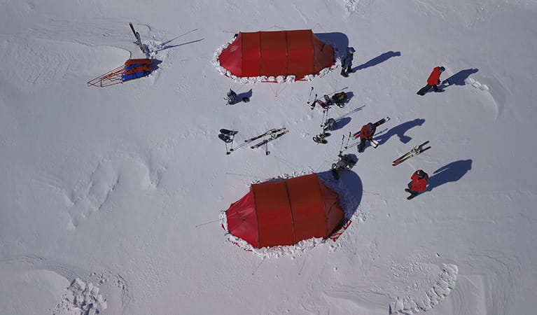 Aerial view of a group of people standing near 2 red tents in a winter snow camp. Photo &copy; Eric Philips