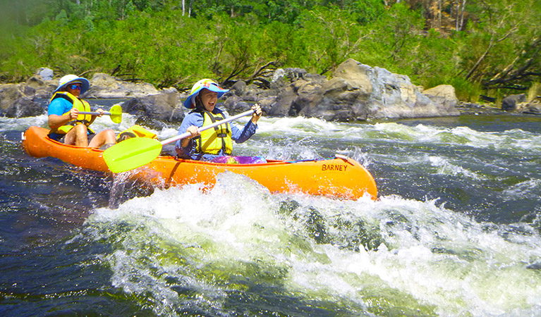 A man and smiling girl in an orange canoe paddle through whitewater along river rapids. Photo &copy; Tegan Cork