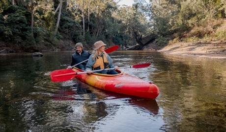 Two people kayaking along Kangaroo River surrounded by bushland and a sandy beach with Kangaroo Valley Kayaks at Morton National Park. Photo: Josh Brnjac &copy; Kangaroo Valley Kayaks