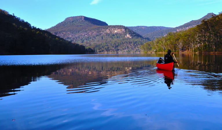 A lone person in a kayak paddles across calm lake waters. Photo credit: Glyn Stones  &copy; Kangaroo Valley Safaris