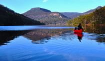 A lone person in a kayak paddles across calm lake waters. Photo credit: Glyn Stones  &copy; Kangaroo Valley Safaris