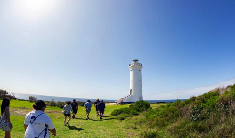 View of people walking over green grass toward the white tower of Point Stephens lighthouse. Photo credit: Bonita Holmes-Nu &copy; Moonshadow-TQC Cruises