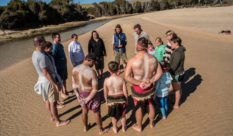 Group of people standing on a sandy beach taking part in Gulaga creation experience. Photo: Ngaran Ngaran Culture Awareness