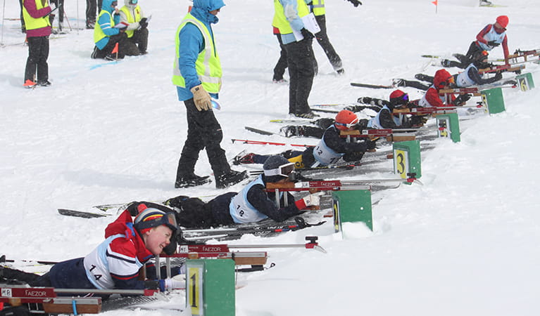 A group of biathlon skiers lie in a line across the snow for target practice, with instructors standing behind them. Photo &copy; NSW Biathlon