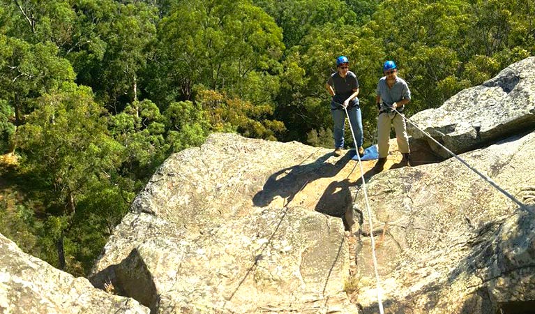 2 people in helmets manage climbing ropes as they stand near the top of a steep rock face. Photo credit: Peter Vaughan © Out and About Adventures