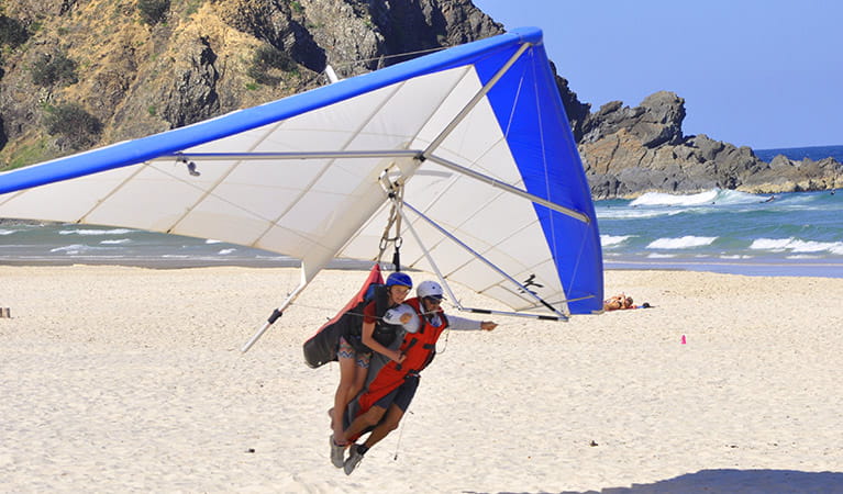 A tandem hang glider about to land on a beach next to to a rocky headland. Photo &copy; Pro Flyte 