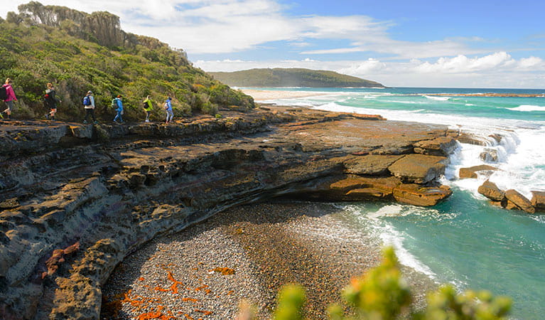 A group of bushwalkers trek toward a rocky point alongside turquoise ocean waters. Photo &copy; Region X