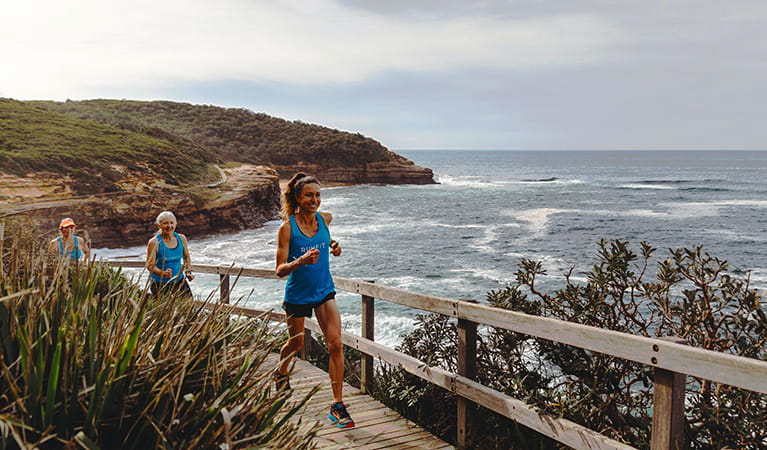A group of runners jogs across a cliffside boardwalk in Bouddi National Park with expansive ocean and coastal views. Photo &copy; Tiffany Alexandria Photography