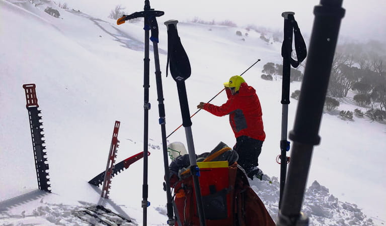 A man in winter outdoor clothing using an avalanche probe on a snow-covered mountain slope. Photo credit: Adam West &copy; Snow Safety Australia