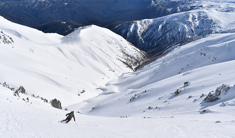 A lone skier descends into a snow-covered mountain valley. Photo credit: Rohan Kennedy &copy; Snowy Mountains Backcountry