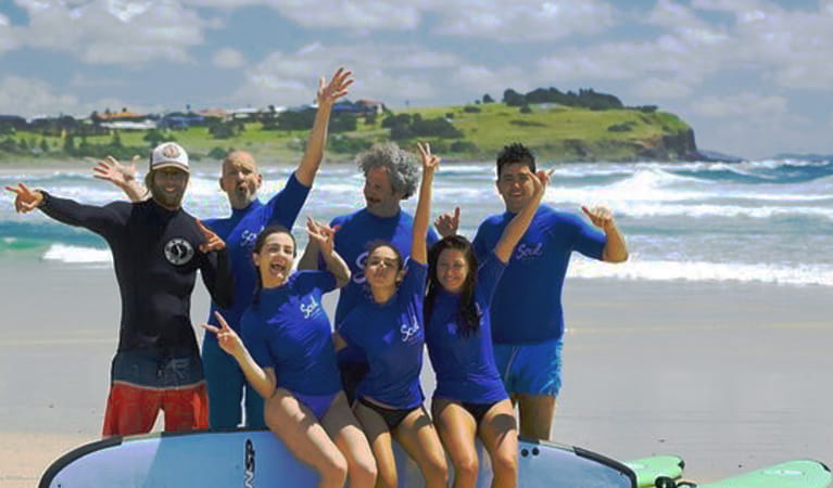 A group of surfers poses for a photo with their Soul Surf School instructor on a beach. Photo credit: Sean Riley &copy; Soul Surf School 