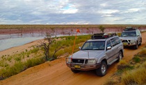 Outback scene with 4WD vehicles driving along a red dirt track past a wetland area. Photo credit: Richard O’Neill &copy; Spirit Safaris