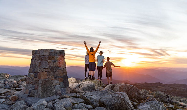 A group of 4 people stand near a rock cairn at the summit of Mount Kosciuszko at sunset. Photo &copy; Thredbo Resort