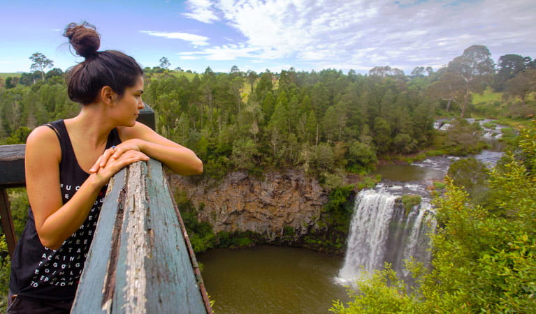 A young woman on a Via Travel Australia guided tour gazes out over a wide vista of bushland, river and waterfall at a lookout. Photo &copy; Via Travel Australia