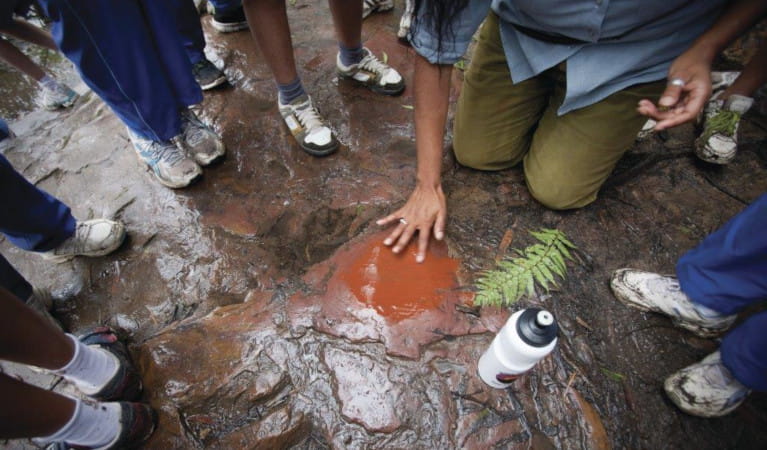 Aboriginal guide mixing red ochre on rocky ground with children's feet surrounding. Photo: Nick Cubbin.