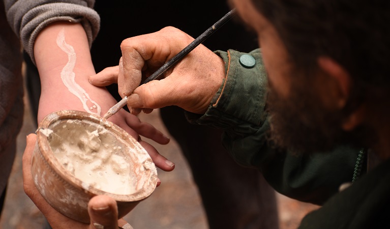An Aboriginal Discovery ranger paints a snake in ochre on a boy's arm. Photo: Paul Watkins/OEH