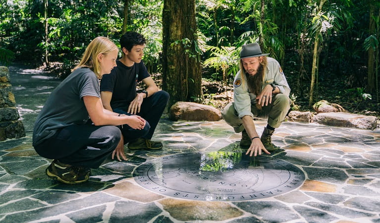 An NPWS ranger and a young woman and man look at the Gondwana circle map on the ground, Dorrigo National Park. Photo: 'And the trees’ Photography &copy; NPWS