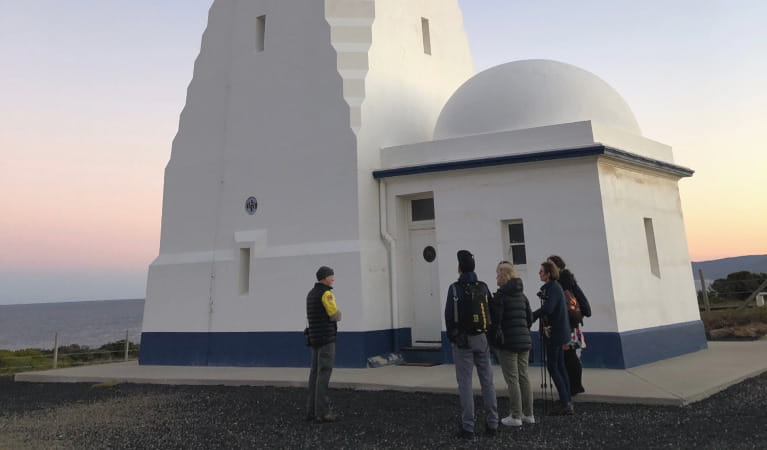 A group of people standing with a guide at the base of Green Cape Lighthouse. Photo: Greg Leary &copy;DPIE