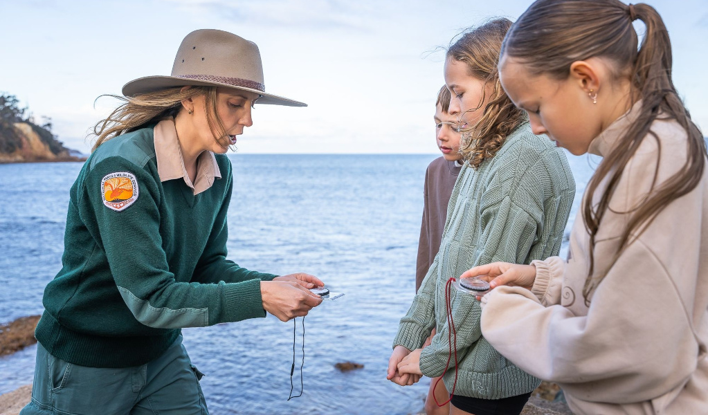 NPWS Ranger shows children a compass in Merimbula National Park. Photo: David Rogers &copy; DCCEEW