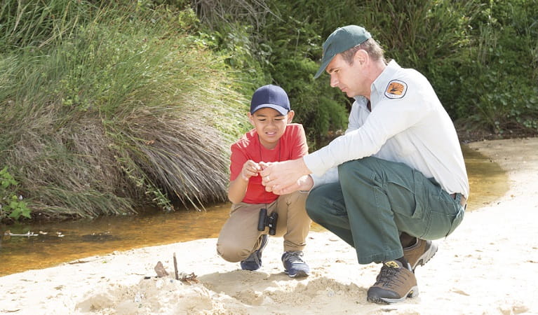 A NSW National Parks ranger and a boy look at a plant by a creek. Photo: Rosie Nicolai/OEH