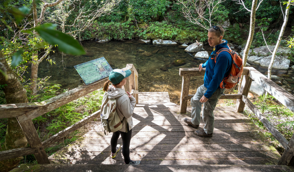 Two walkers take a break next to stream in Washpool National Park. Photo: David Waugh &copy; DPE