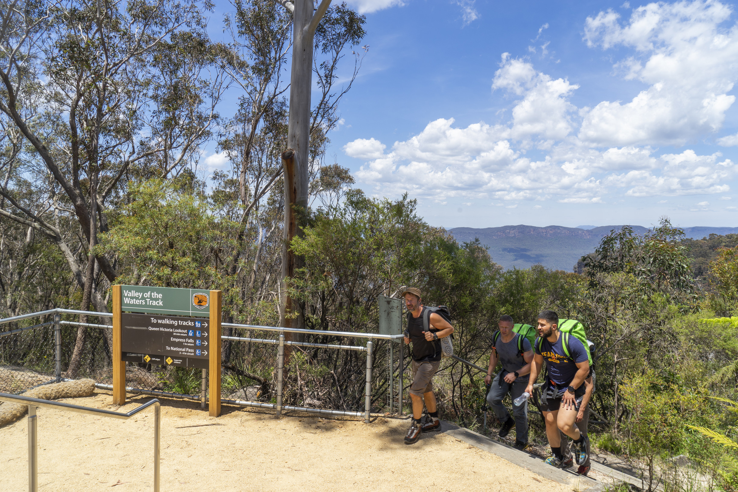 Three hikers with backpacks reach the top of a long set of stops in the Blue Mountains. Credit: Simone Cottrell &copy;  Simone Cottrell/DCCEEW