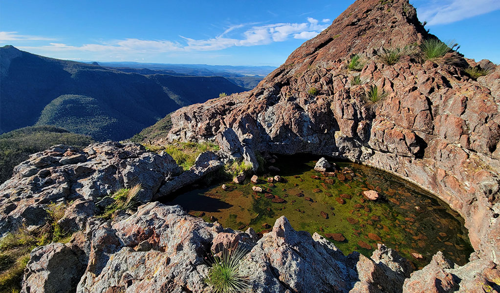 Small clear lake surrounded by a large colourful rock on top of a mountain. Credit: James Hastings/DPE