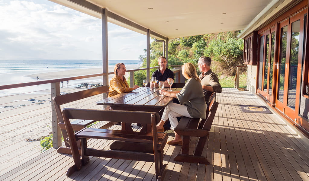 A group sitting around an outdoor table at Imeson Cottage beachfront accommodation in Byron Bay. Credit: Sera Wright &copy; DPE