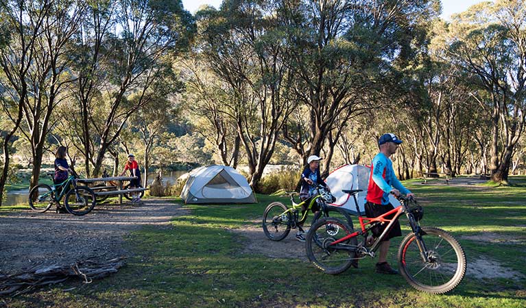 A family walk their mountain bikes past tents at Thredbo Diggings campground in Kosciuszko National Park. Photo: Robert Mulally/DPIE
