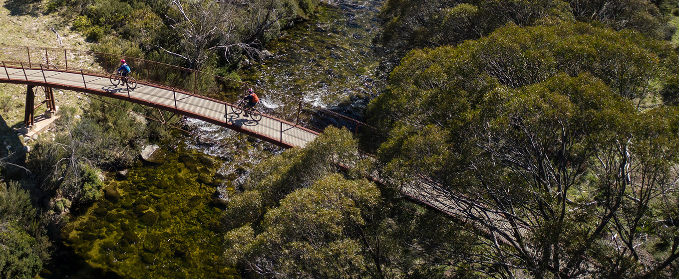 Aerial view of two mountain bike riders crossing a bridge over the Thredbo River on Thredbo Valley track, Kosciuszko National Park. Photo: Robert Mulally/DPIE