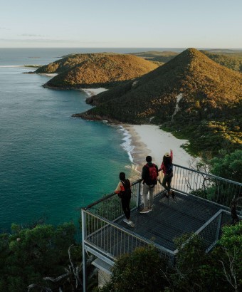 Three people stand at the summit of Tomaree Head, looking at the coastline. Credit: Daniel Parsons &copy; Daniel Parsons