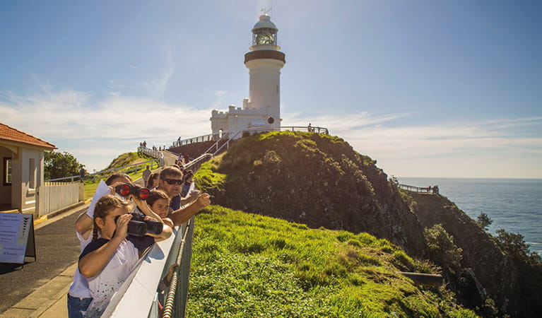 A group of people with binoculars watch for whales, with Cape Byron lighthouse in the background.  Photo credit: John Spencer &copy; DPIE