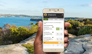 A hand holds a mobile phone with water views background from Sydney Harbour National Park. Photo: Simone Cottrell &copy; DPIE