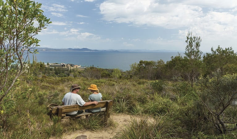Visitors sitting on a bench chair on Monument Hill walking track, Arakoon National Park. Photo: David Finnegan/DPIE