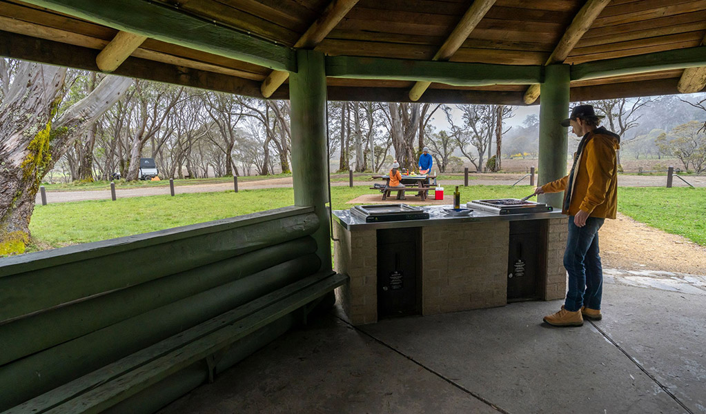 A person using a barbecue in a covered pavilion with views out to a picnic table in Polblue campground and picnic area. Credit: John Spencer/DCCEEW  &copy; DCCEEW