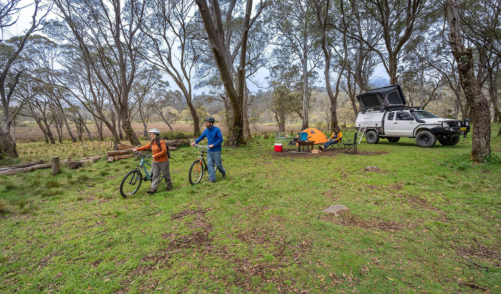 2 people walking mountain bikes from their campsite in Polblue campground and picnic area. Credit: John Spencer/DCCEEW  &copy; DCCEEW