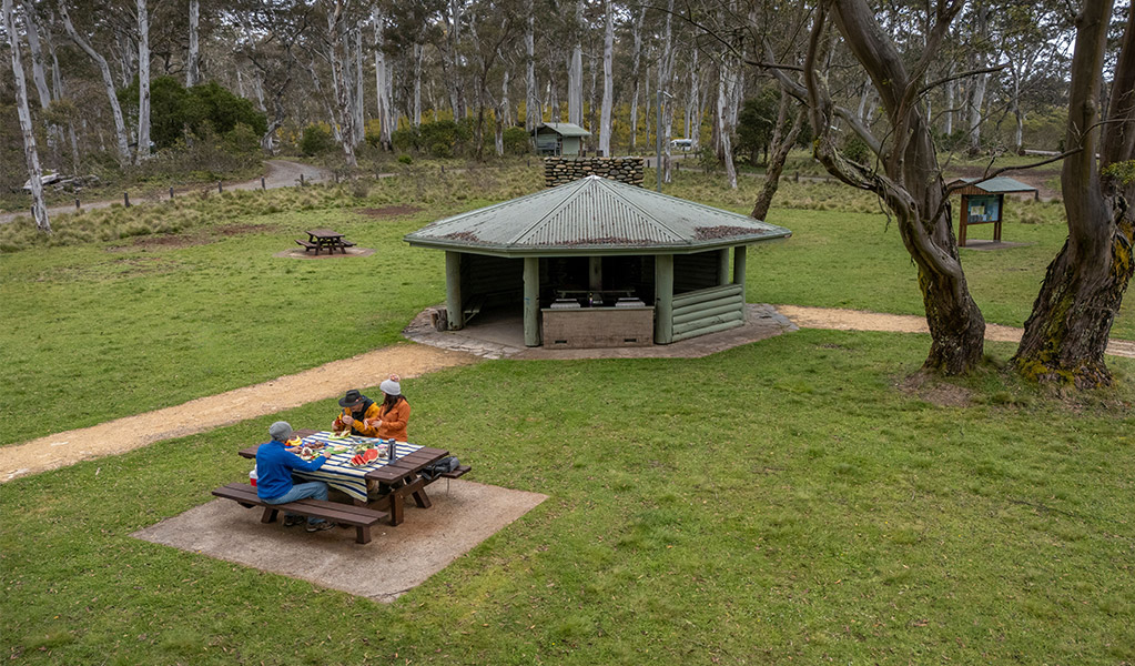 2 people eating at a picnic table near barbecue facilities under a covered pavilion in Polblue campground and picnic area. Credit: John Spencer/DCCEEW  &copy; DCCEEW