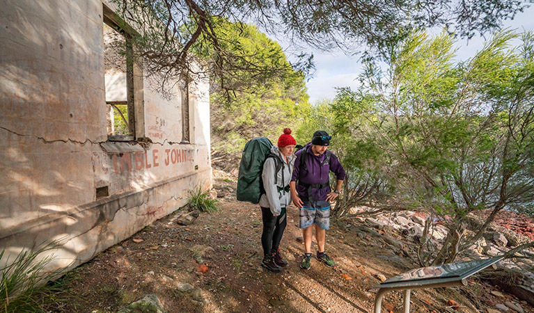 People doing the Light to Light walk stop to read an information sign at Bittangabee Bay Storehouse. Photo: John Spencer/OEH