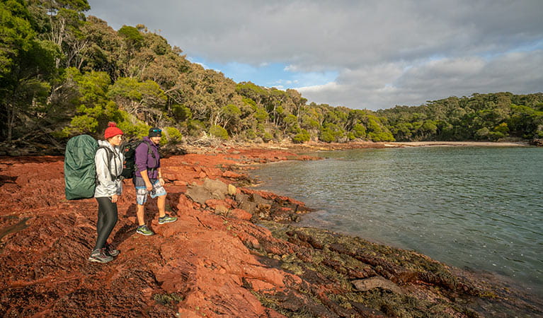 Light to Light walkers standing on the red rocks at Bittangabee Bay. Photo: John Spencer &copy; OEH