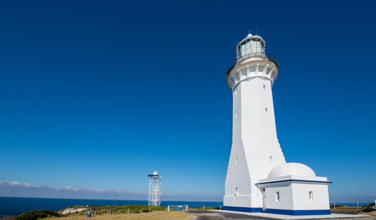 View of Green Cape Lighthouse on a grassy flat with the ocean in the background. Photo: John Spencer &copy; DPIE