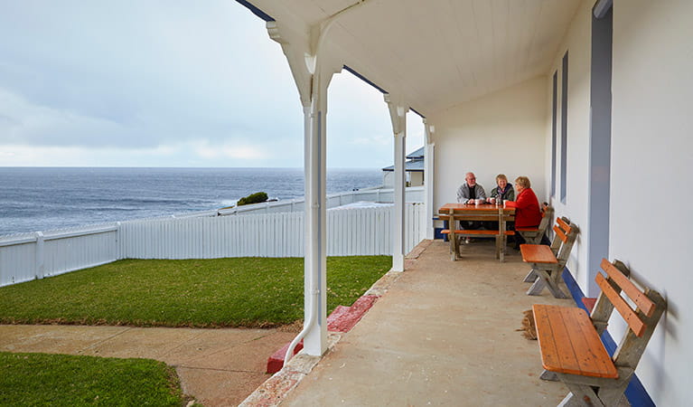 Friends sitting on the verandah with views of the ocean at Green Cape Lightstation Keeper's Cottage in Beowa National Park. Photo: Nick Cubbin/OEH