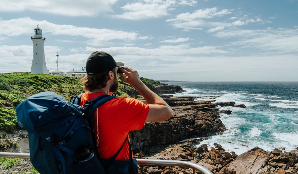  Visitor gazing through a pair of binoculars towards the vast expanse of rugged coastline at Green Cape lookout. Credit: Daniel Parsons/DCCEEW &copy; Daniel Parsons