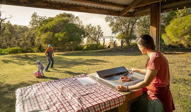 A woman cooks some sausages on the grill, Haycock Point picnic area, Beowa National Park. Photo: John Spencer/OEH