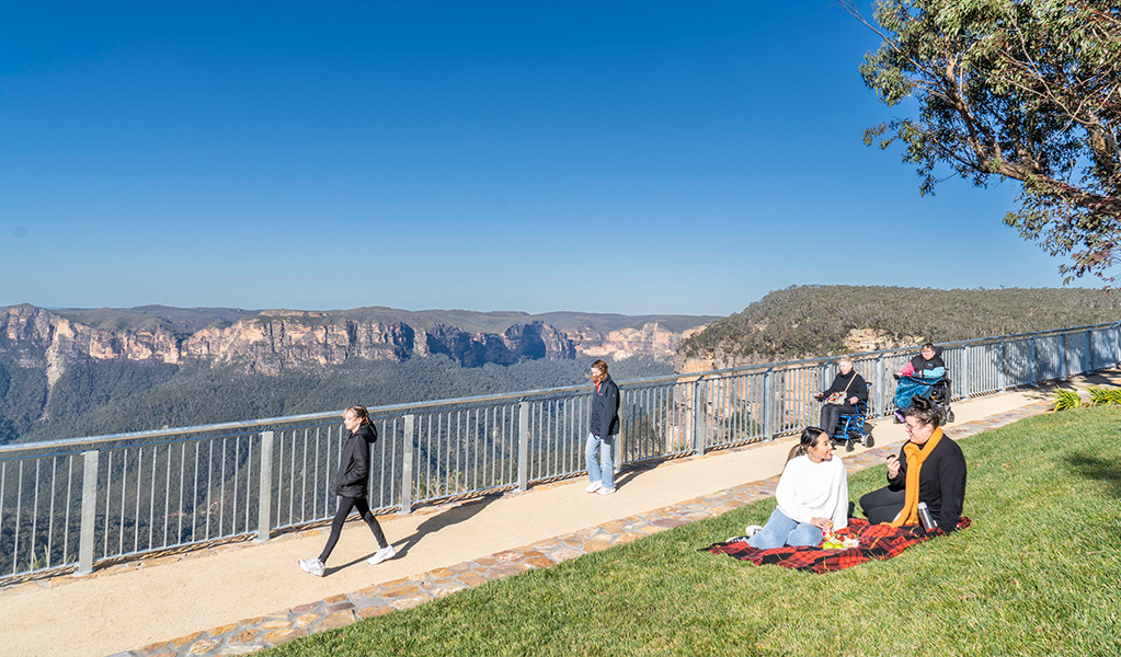 Visitors using an accessible path and having a picnic on the grass at Govetts Leap lookout. Credit: Simone Cottrell/DPE &copy; DPE