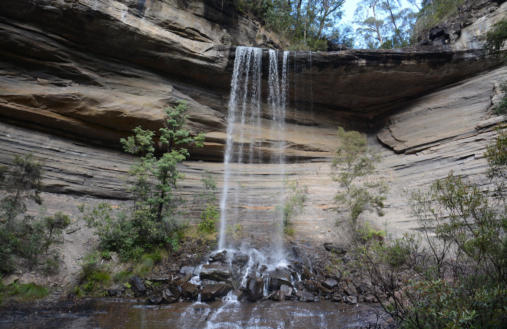 Sandstone cliffs, with a view of Victoria Creek cascading over a rock shelf and onto rocks below. Photo: Grant Purcell &copy; DPIE