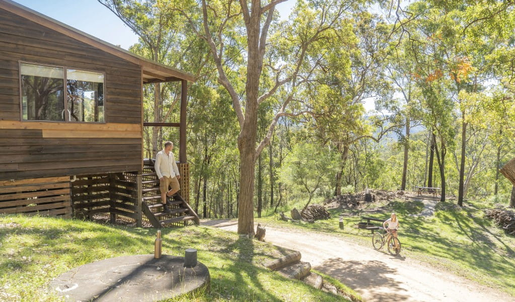 A man standing on the stairs of Galong cabins talking to a woman wheeling a bicycle along a path in Blue Mountains National Park. Photo: Simone Cottrell &copy; DPIE