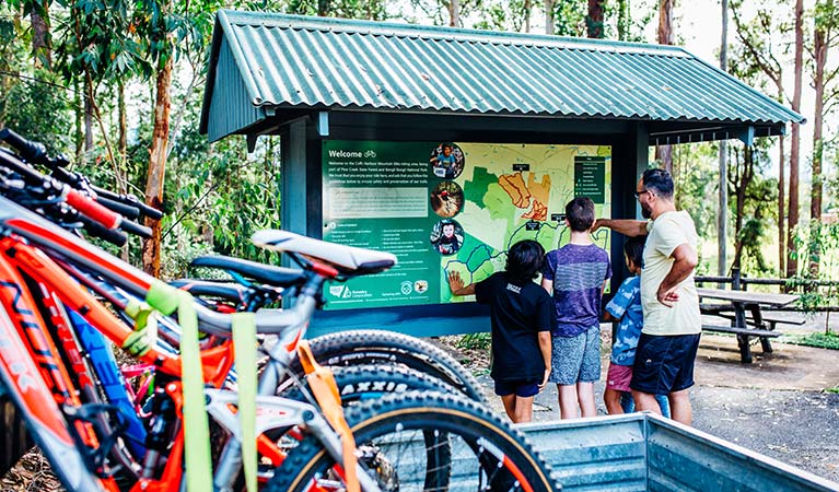 A man and 3 children look at a map at an information bay, with mountain bikes in the foreground. Photo: Jay Black/DPIE
