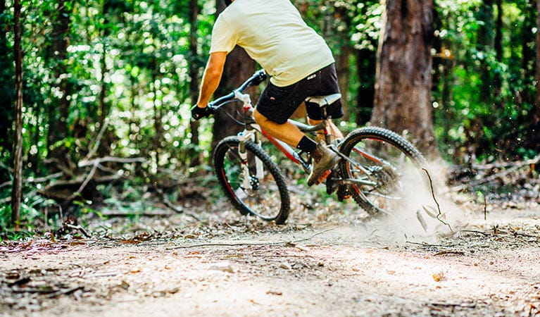 A man on a mountain bike corners on a dirt trail, kicking up dust. Photo: Jay Black/DPIE