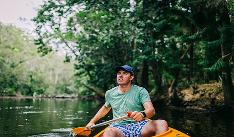 A man paddling a canoe along Pine Creek, with creek banks in distance. Photo: Jay Black &copy; OEH