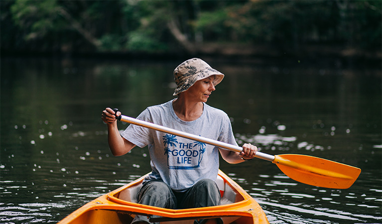 A woman paddling an orange canoe on Pine Creek, with creek bank in background. Photo: Jay Black &copy; OEH